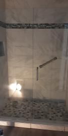 A glass shower enclosure with a diagonal metal grab bar and a mosaic tile floor.