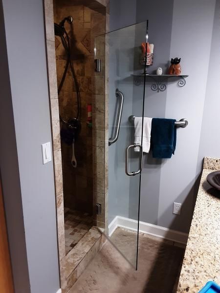 A walk-in shower with a glass door, grab bar, and wall-mounted towel rack in a neutral-toned bathroom.