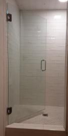 A glass shower door with a metal handle and hinges installed over a white tiled shower floor.