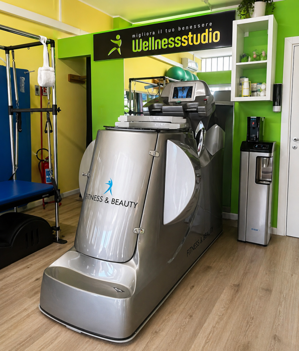 Palestra al coperto con una macchina Pilates reformer, una panca nera e attrezzature per esercizi colorate in una stanza luminosa.