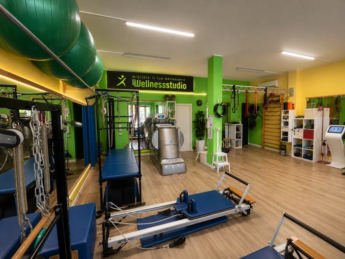 Palestra domestica con attrezzatura Pilates reformer, pavimento in legno e colorati quadri alle pareti.