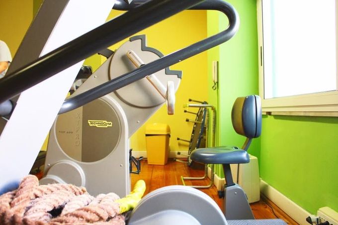 Sala fitness con attrezzi ginnici, una sedia blu e pareti giallo brillante vicino a una finestra