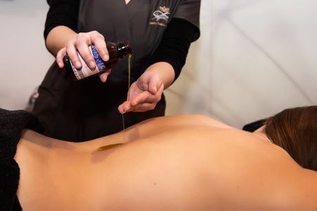 Un massaggiatore versa dell'olio da massaggio sulla schiena di un cliente sdraiato su un lettino da massaggio.