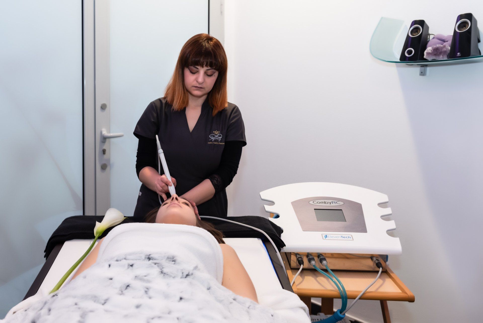 Un tecnico utilizza un dispositivo cosmetico portatile su una cliente sdraiata su un lettino da trattamento in una sala spa.