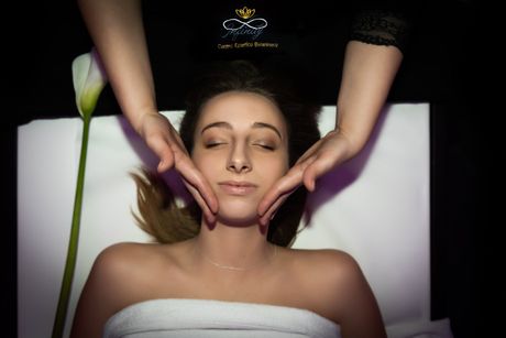 Una persona riceve un massaggio facciale rilassante, a occhi chiusi, con un fiore bianco e luci soffuse in un ambiente spa.