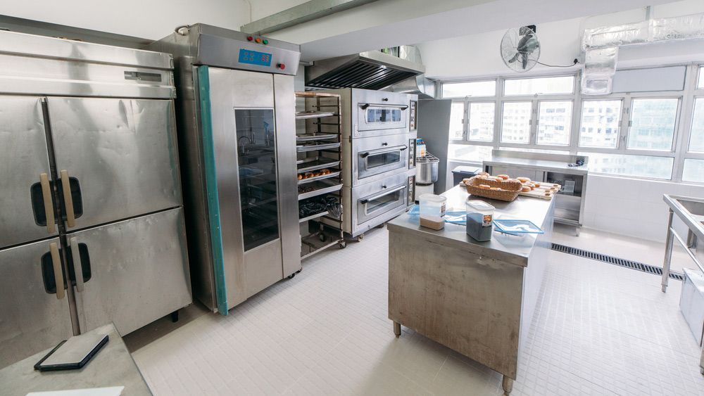 A Kitchen With a Lot of Stainless Steel Appliances and a Table — Commercial Kitchens Direct in Unanderra, NSW