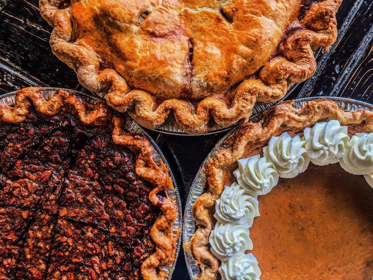 Three different types of pies are sitting on a wooden table.