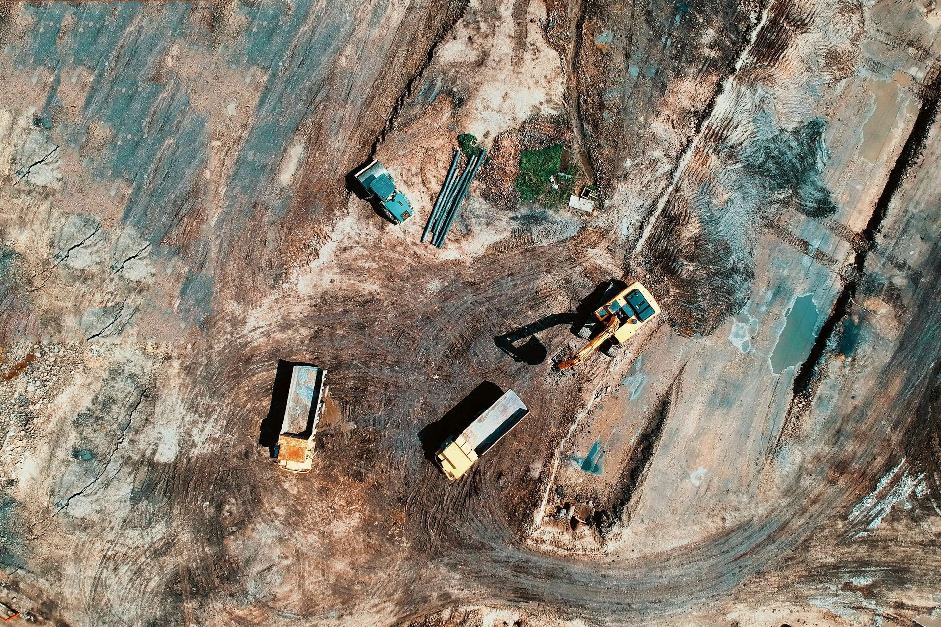 Aerial view of a construction site with trucks and an excavator in shades of brown and gray.