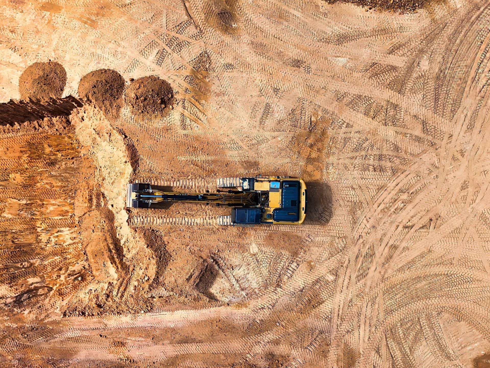 Aerial view of a blue truck on a dirt road beside several hay bales in a field