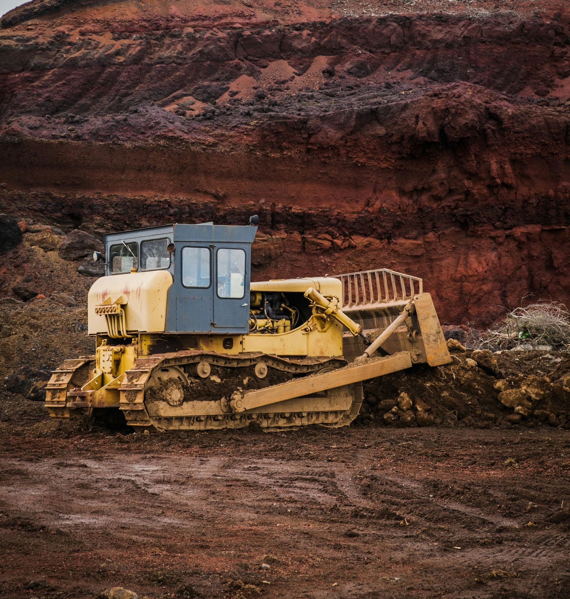 Yellow bulldozer in a reddish-brown dirt quarry, pushing soil.