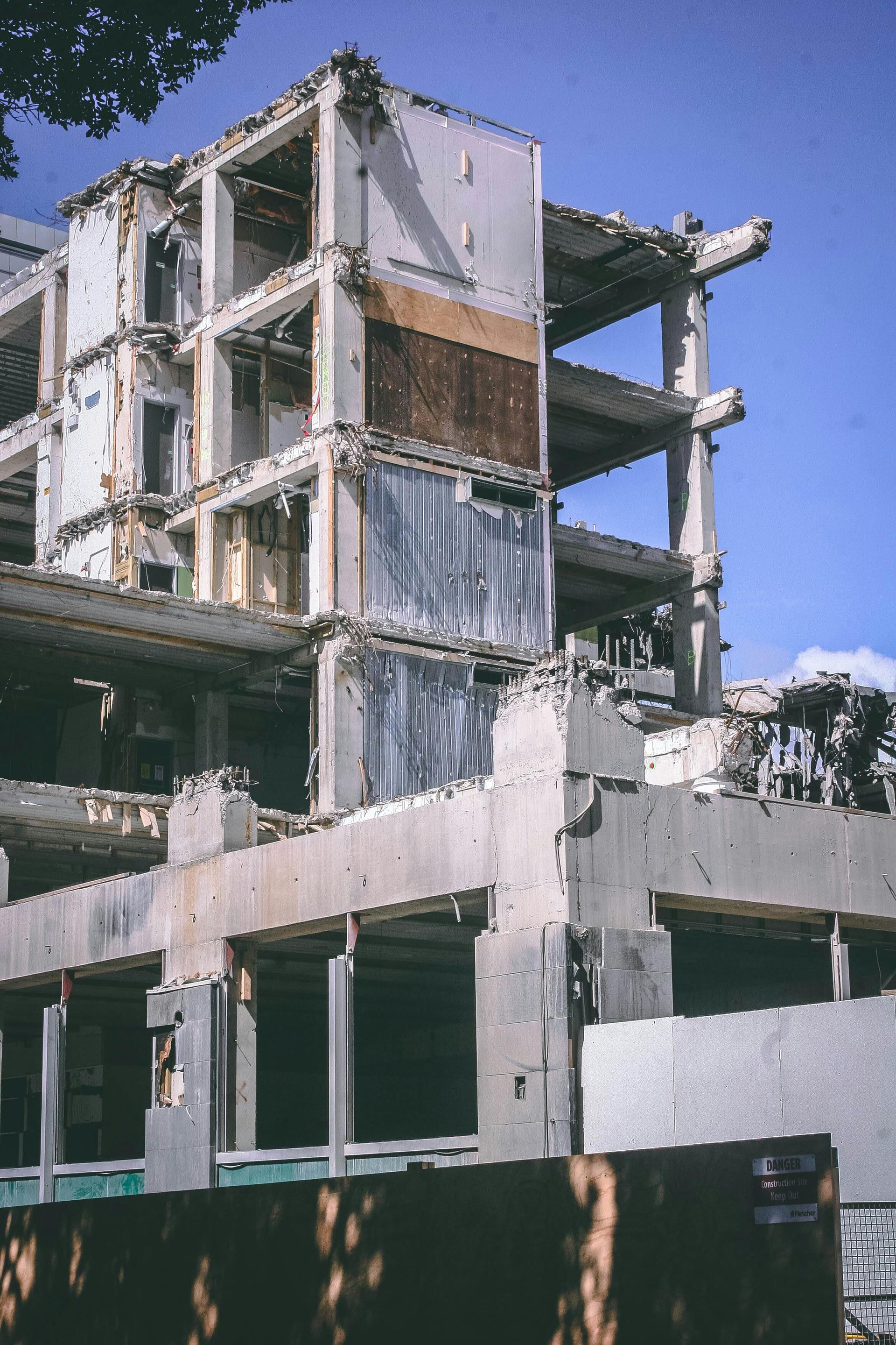 Demolished concrete building with exposed floors and sections. Light blue sky in the background.