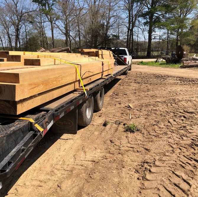 A truck is carrying wooden beams on a trailer.