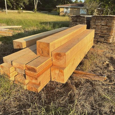 A pile of wood sitting in the grass with a house in the background