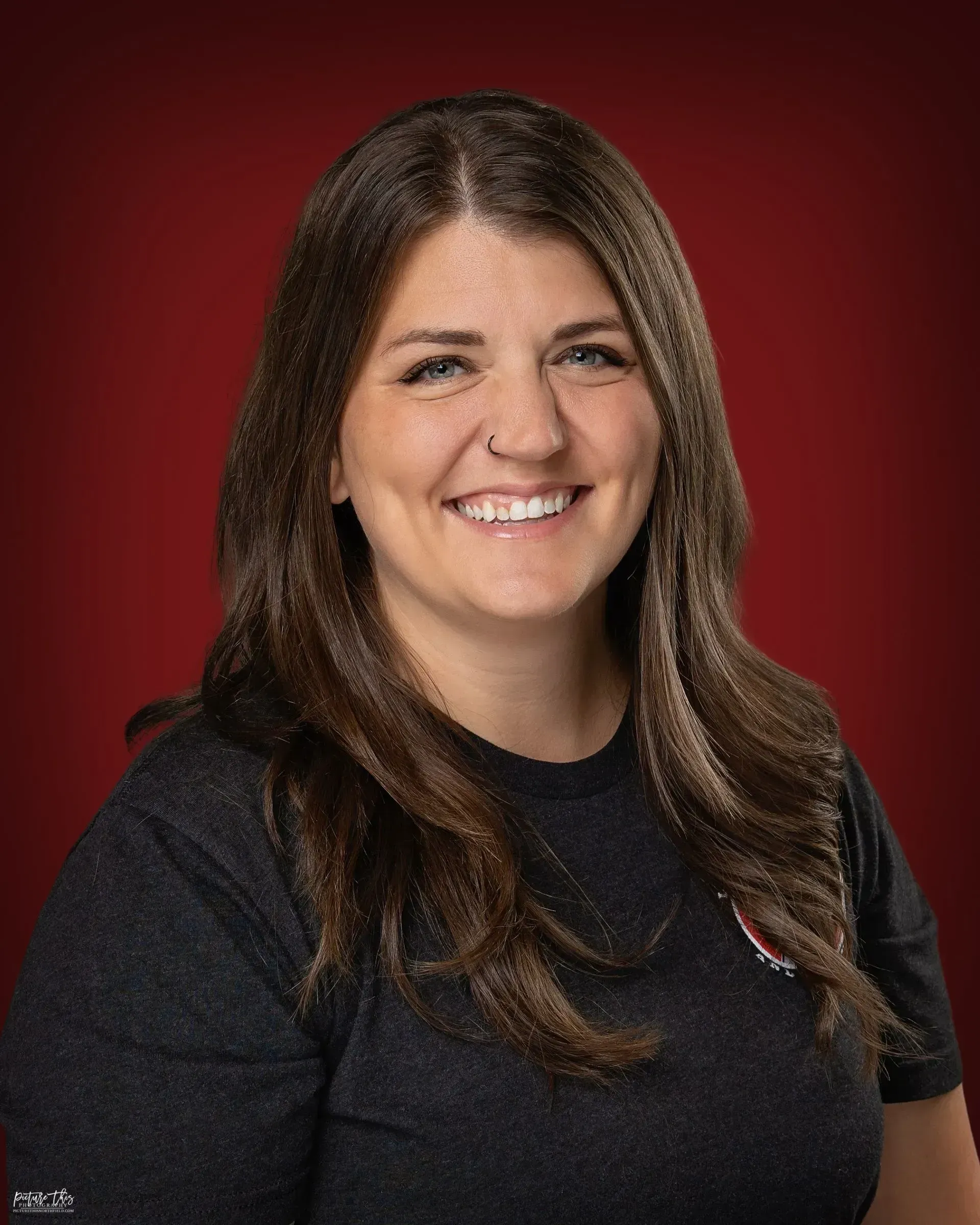 Smiling woman in a black top against a dark red studio background.