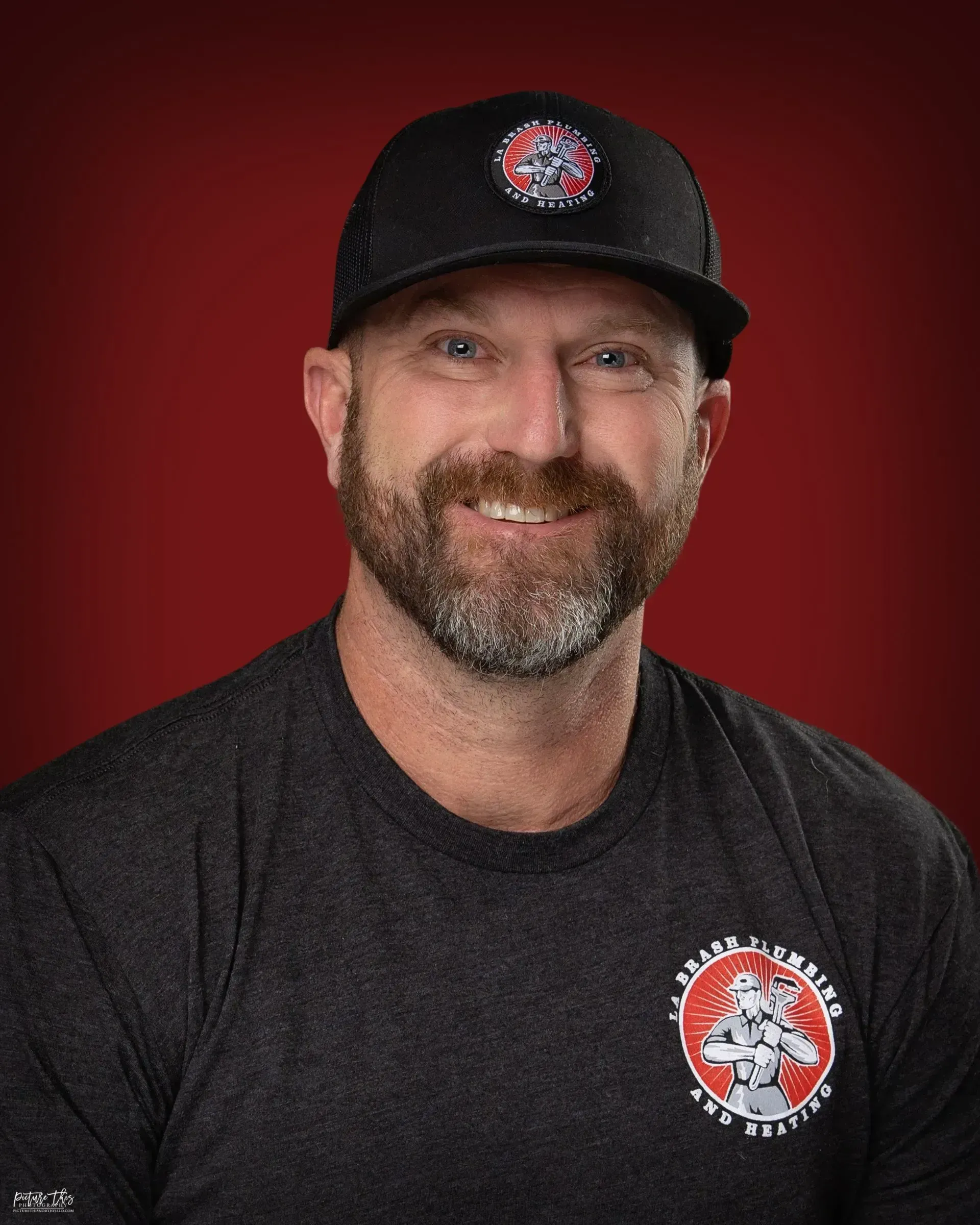 Smiling man in black cap and shirt with a red logo on a red background