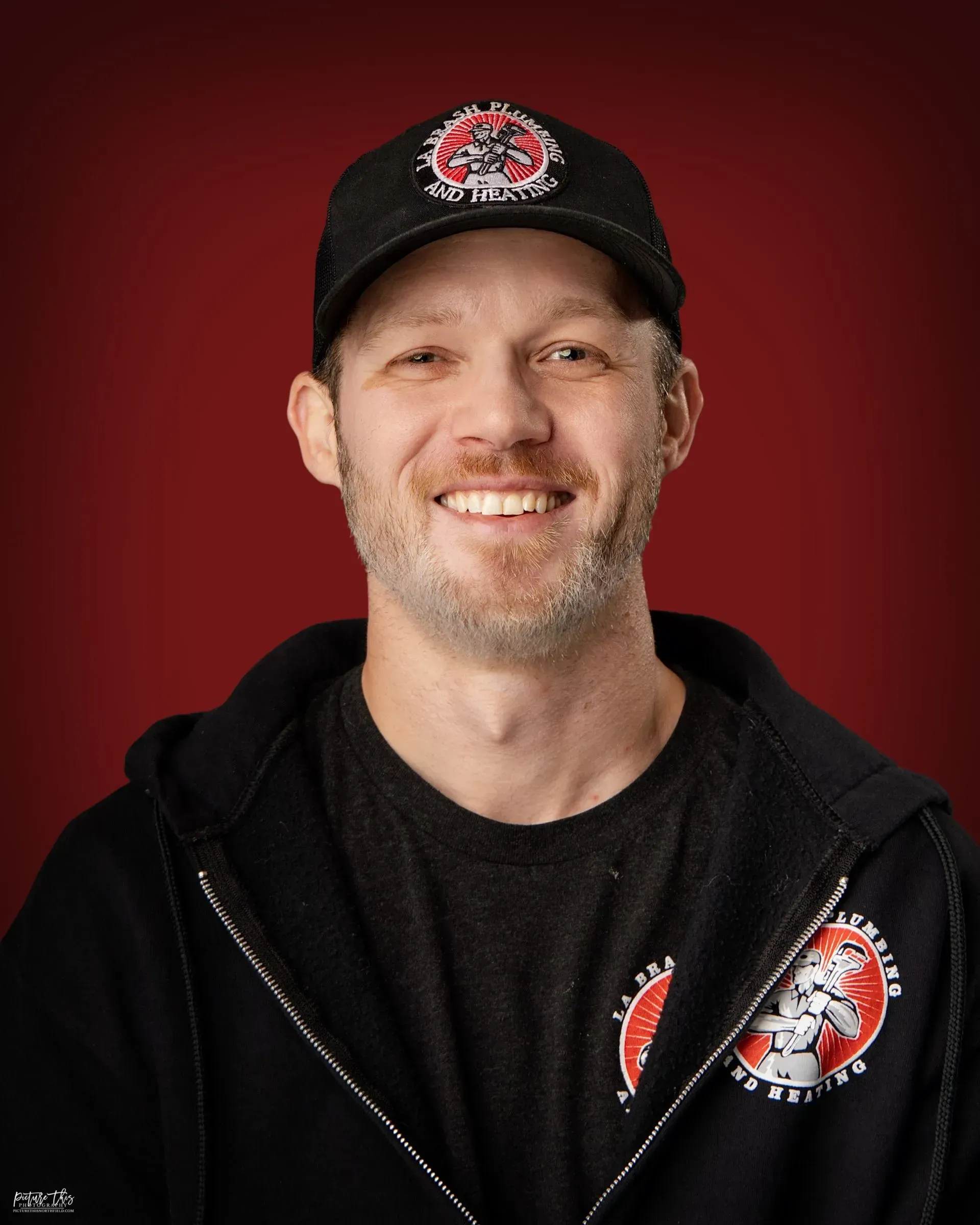 Smiling man in black cap and jacket against a red background