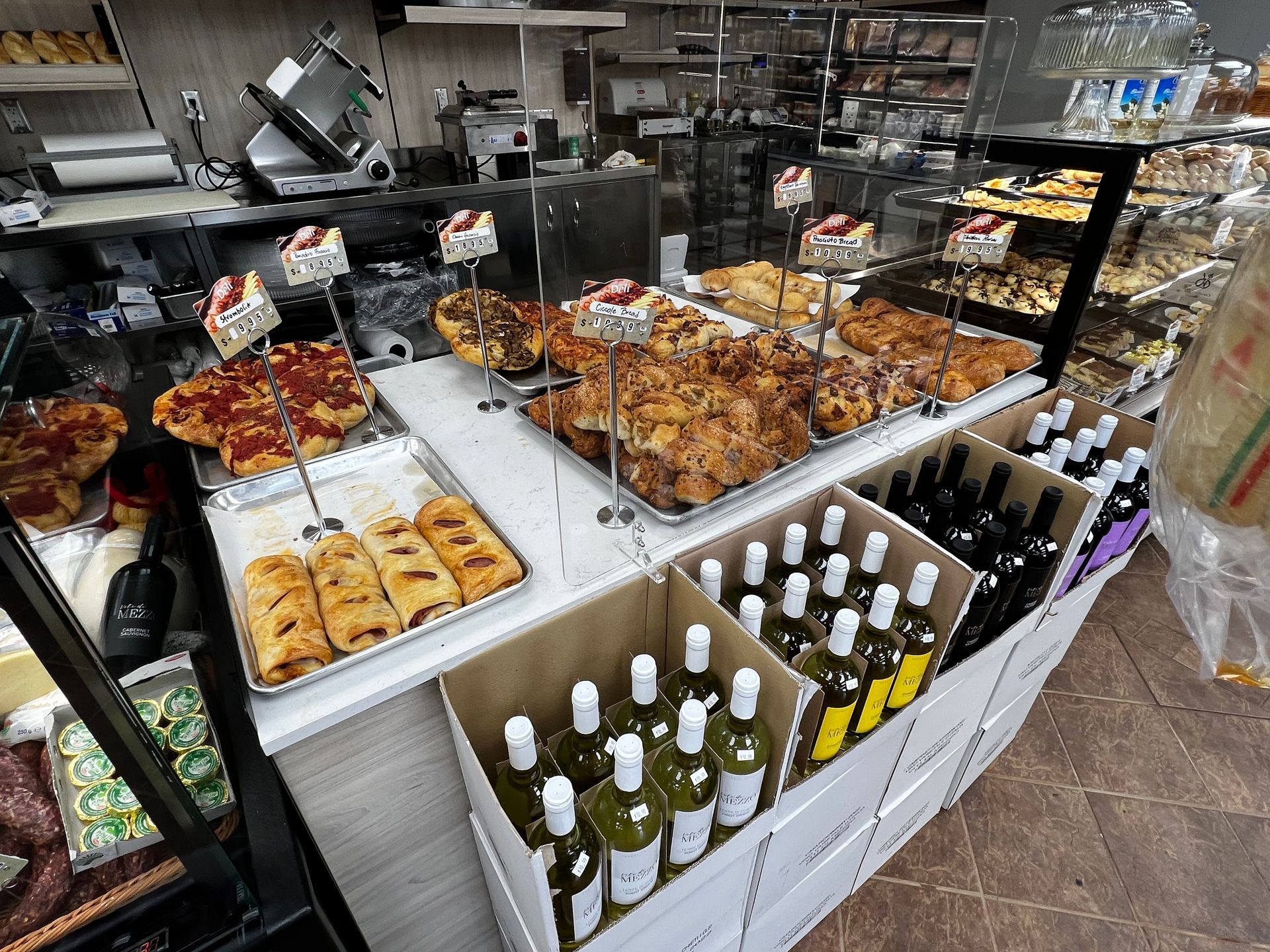A bakery with lots of food and bottles of wine