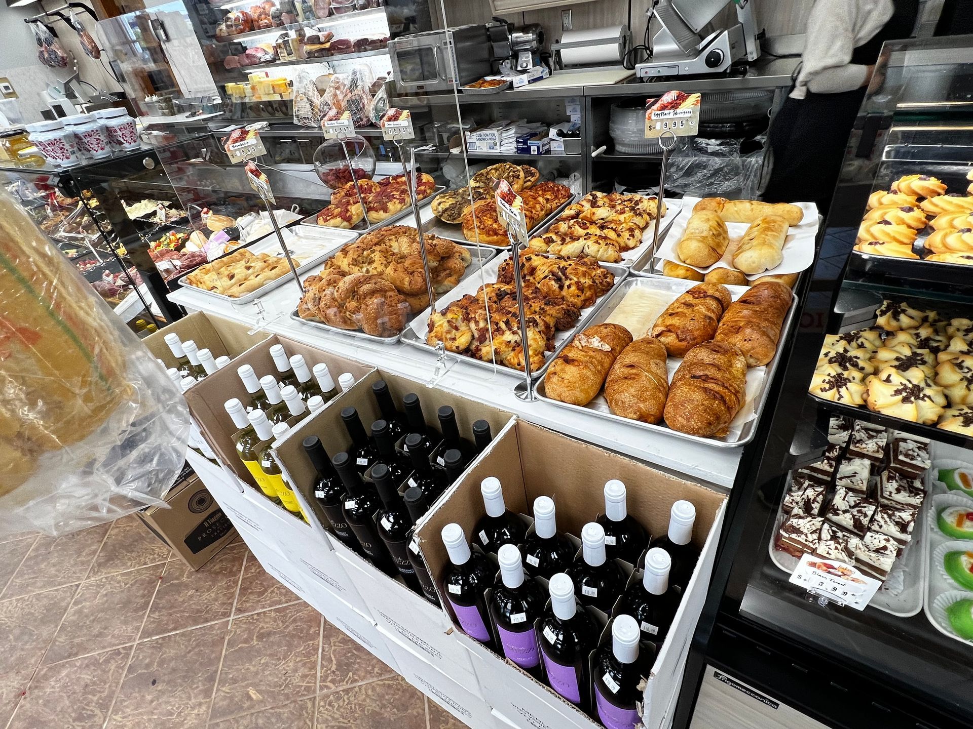 A bakery display case filled with lots of food and wine bottles.