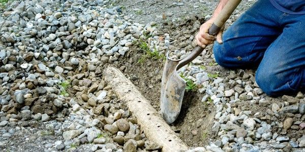 Une personne creuse à la pelle à côté d'un tuyau perforé dans une tranchée remplie de gravier.