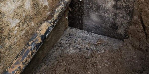 Gros plan sur un coin sombre et usé par les intempéries, avec un objet noir ressemblant à un tuyau qui longe un côté.
