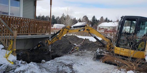 Une pelleteuse jaune creuse à côté d'une maison, le sol étant enneigé.