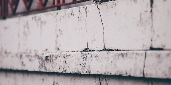 Gros plan sur un mur de briques blanches patiné par le temps, présentant des taches sombres et une rambarde rouge en arrière-plan.