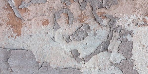 Gros plan sur un mur abîmé par les intempéries, dont la peinture s'écaille dans des tons beige, gris et brun.