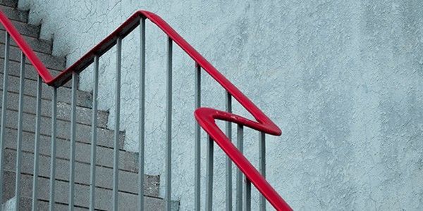 Une rampe rouge serpente le long d'un escalier métallique, adossé à un mur gris texturé.