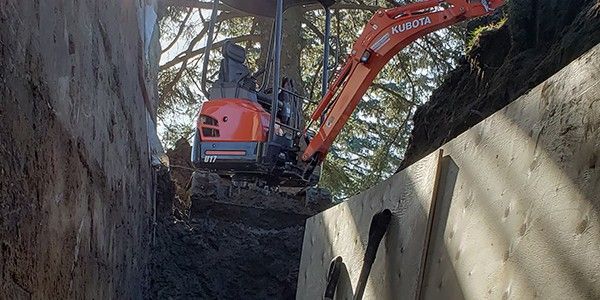 Une pelle mécanique Kubota orange creuse une tranchée près d'un mur en bois.