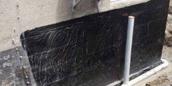 Membrane d'étanchéité noire sur un mur de fondation avec un tuyau.