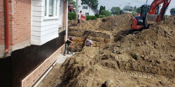 Excavation des fondations d'une maison à l'aide d'une excavatrice et d'ouvriers.