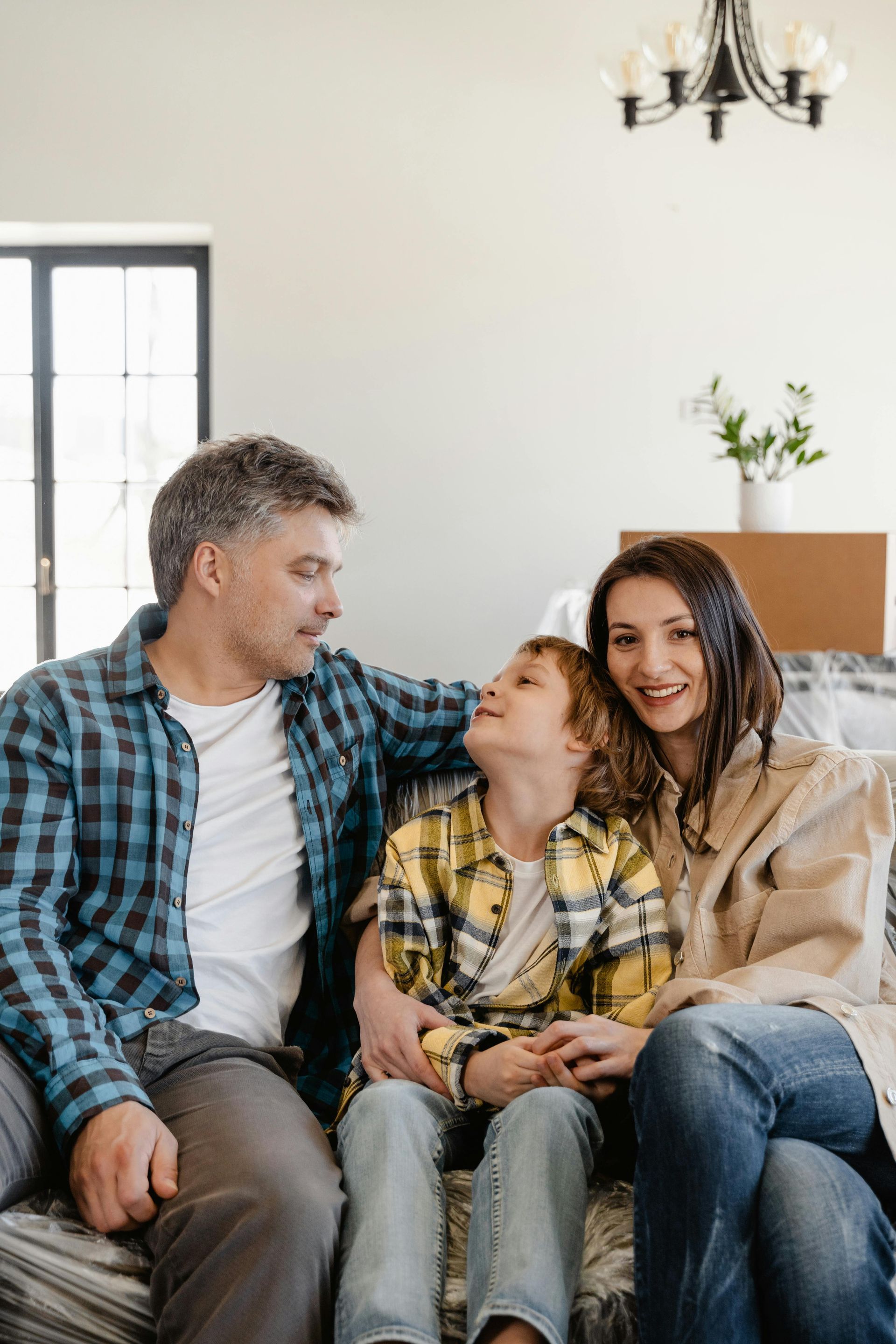 A family of three sitting together on a couch, smiling at each other in a bright, modern room.