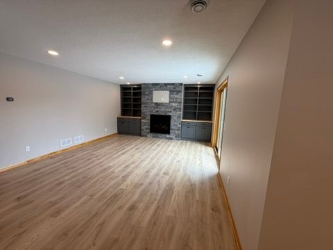 Empty living room with light wood floors, white walls, and a dark stone fireplace.