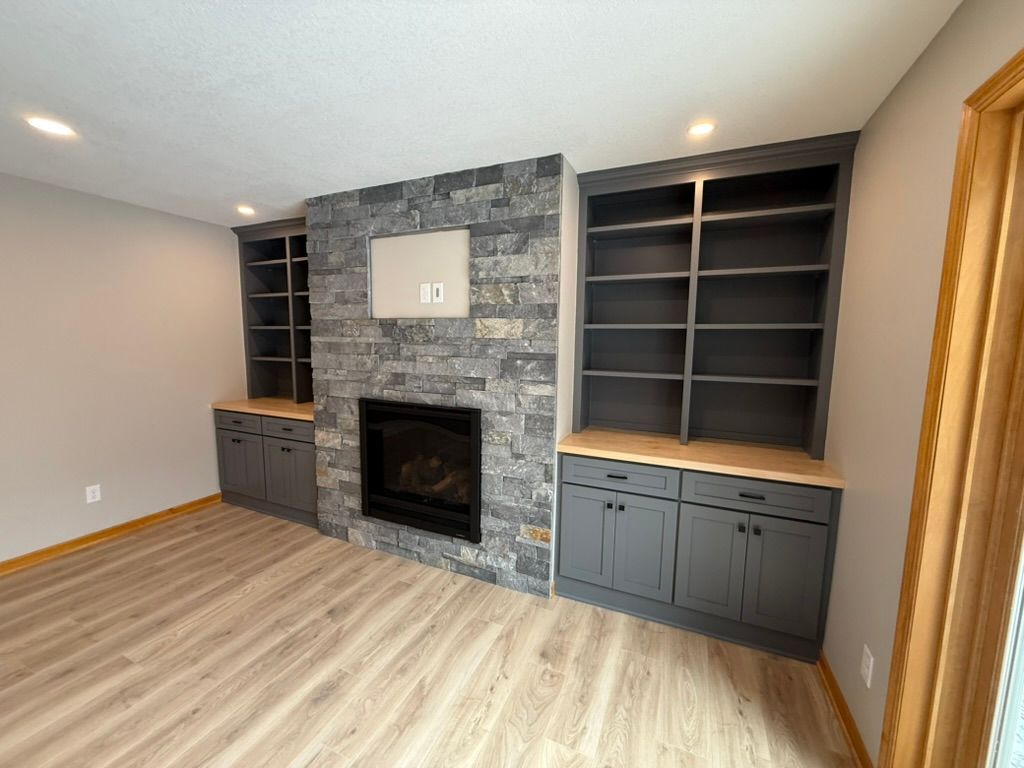 Empty living room with gray stone fireplace and built-in dark shelving and cabinets