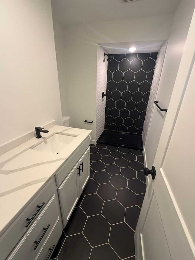 Narrow bathroom hallway with white vanity and black hexagon tile floor leading to a dark hexagon-tiled shower curtain.