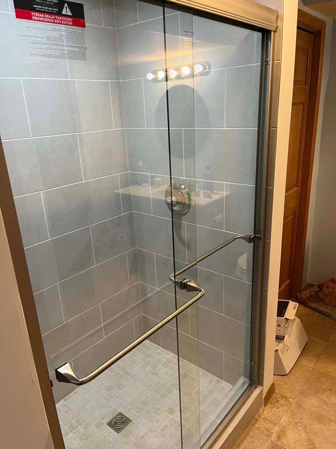 Glass shower stall with chrome grab bar and tile walls in a bathroom