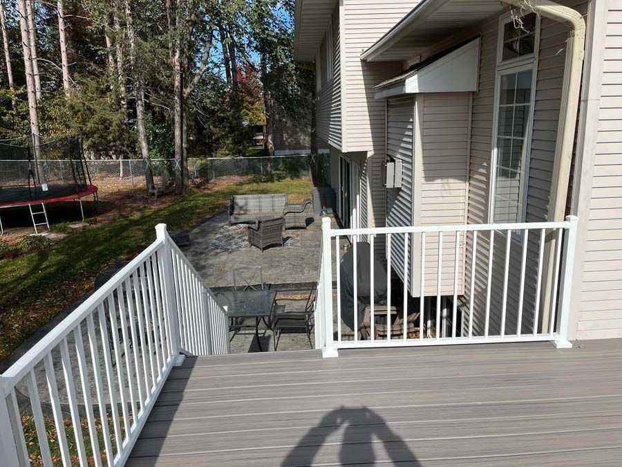 Deck overlooking a backyard with patio chairs, a fire pit, and a trampoline among trees