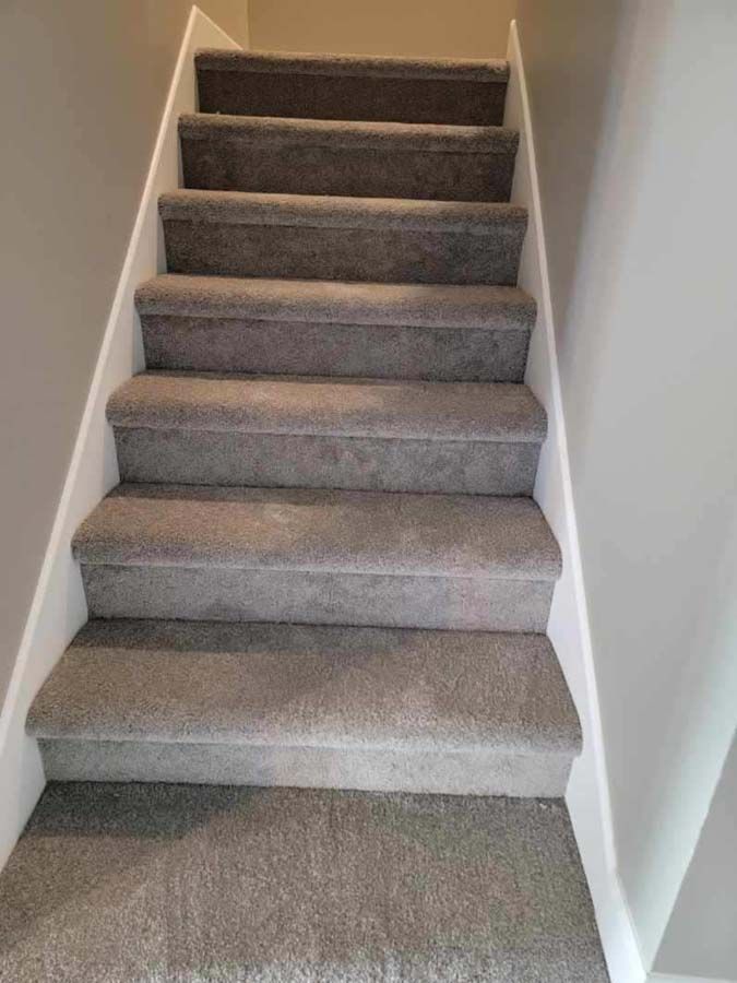 Carpeted indoor staircase with white walls, viewed from the bottom looking up
