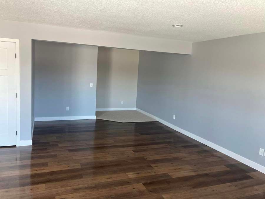Empty room with gray walls, dark wood floors, white trim, and a small entry area.