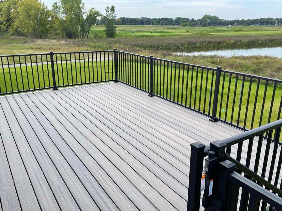 Black deck with railing overlooking a marsh and pond under a clear sky