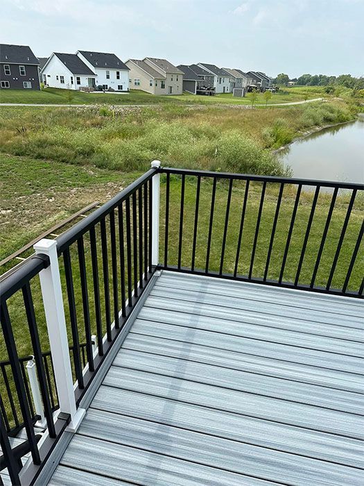 Wooden deck overlooking grassy marsh and pond, with houses in the distance under a cloudy sky