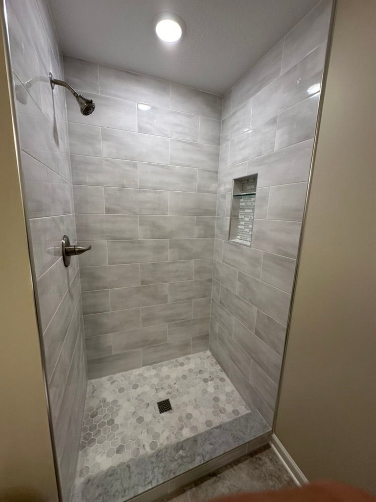 Tiled walk-in shower with gray walls, small mosaic floor, glass door, and wall niche.
