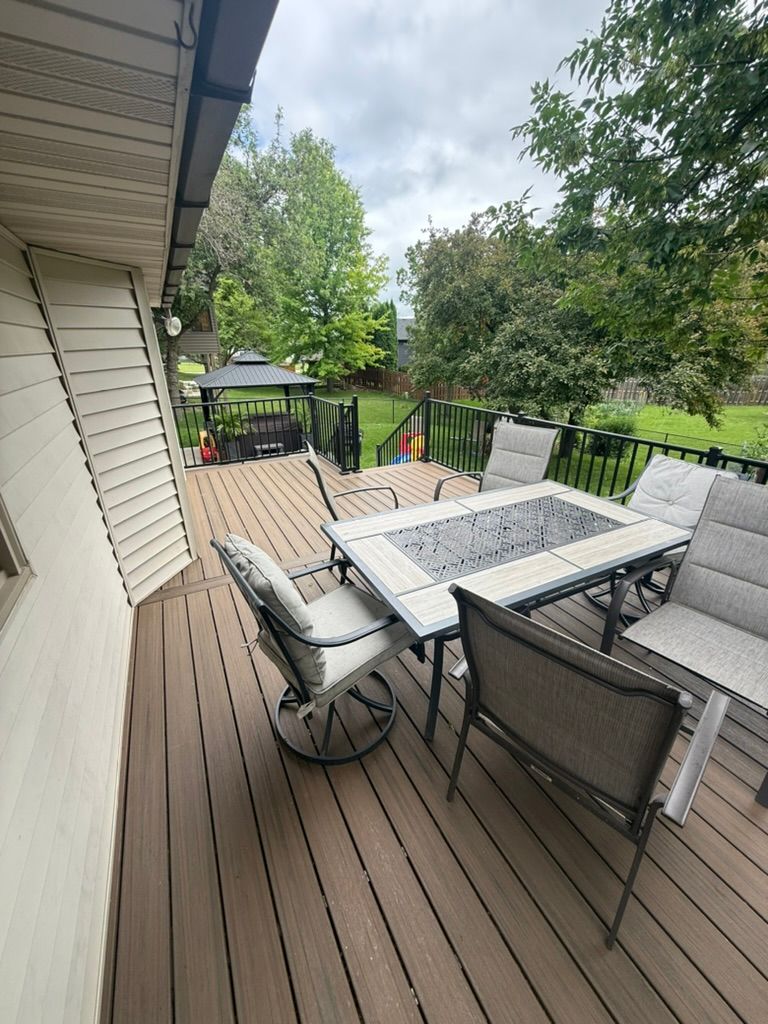 Wooden deck with outdoor dining table and chairs, overlooking a green backyard and trees.