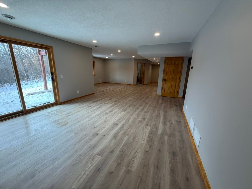 Empty modern living room with light wood floors, recessed lights, and large sliding glass doors.