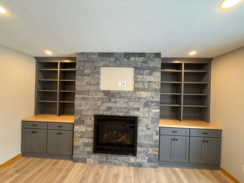 Living room fireplace with stone surround, built-in shelves, and gray cabinets on both sides
