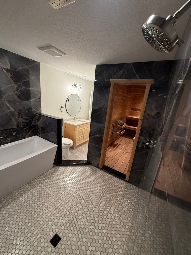 Bathroom with tub, mosaic tile floor, round mirror, and open wooden sauna door.
