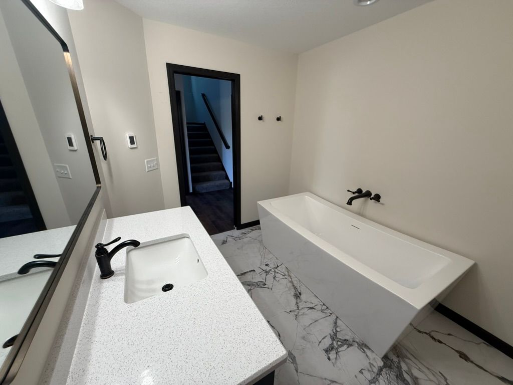 Modern bathroom with white vanity, black fixtures, and freestanding tub near an open doorway.