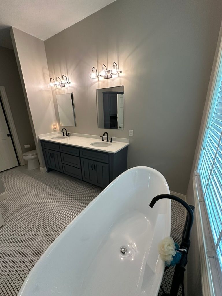 Modern bathroom with double vanity, lit sconces, mirror, and freestanding tub in foreground
