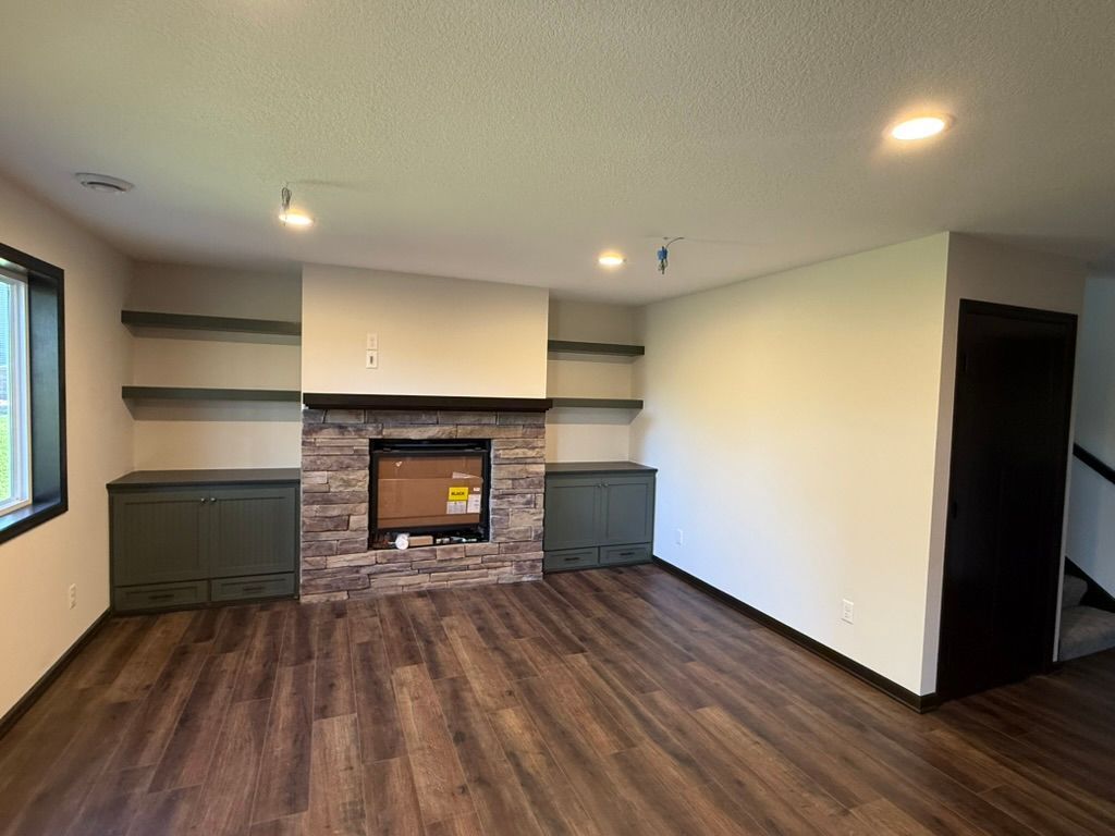 Empty living room with dark wood floors, fireplace, built-in shelves, and large windows