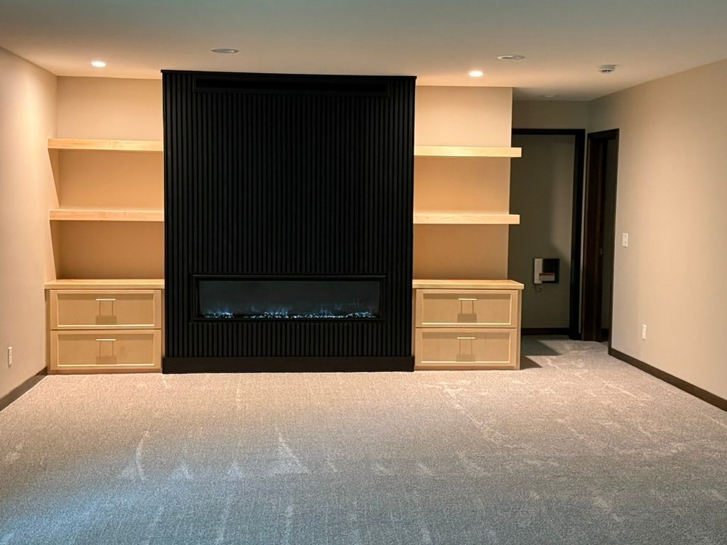 Empty living room with built-in shelves and cabinets framing a black modern fireplace.